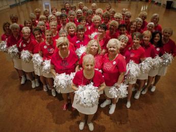 Photo of a cheerleader group composed of elderly women, all in red tops and white skirts, with pompoms