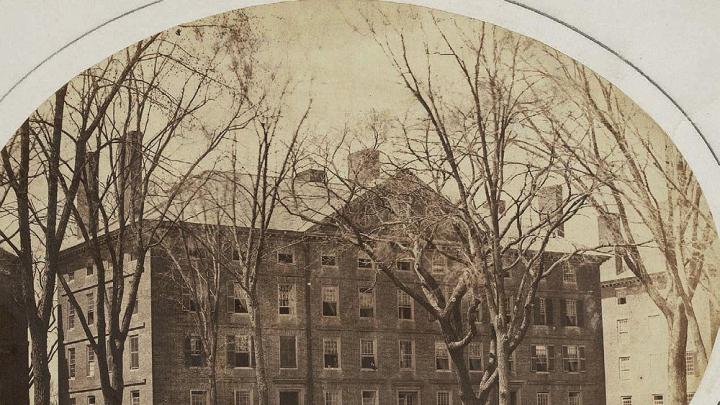 Old photograph of Hollis Hall with students gathered around the large “Rebellion Tree” in front of the building.