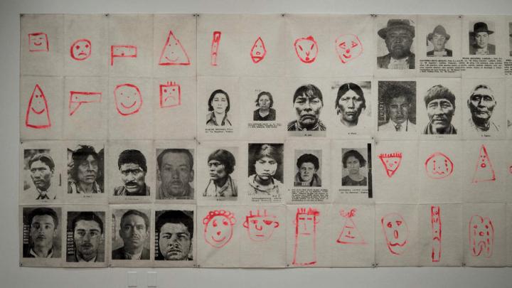 A grid comprised of 48 portraits, including black-and-white photographs of South American indigenous people and criminal mugshots, and simple, childlike drawings of human faces in bright red