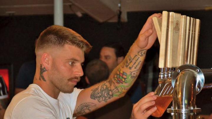 Handsome, tattooed bartender at Provincetown Brewing Company tapping craft beer for a customer